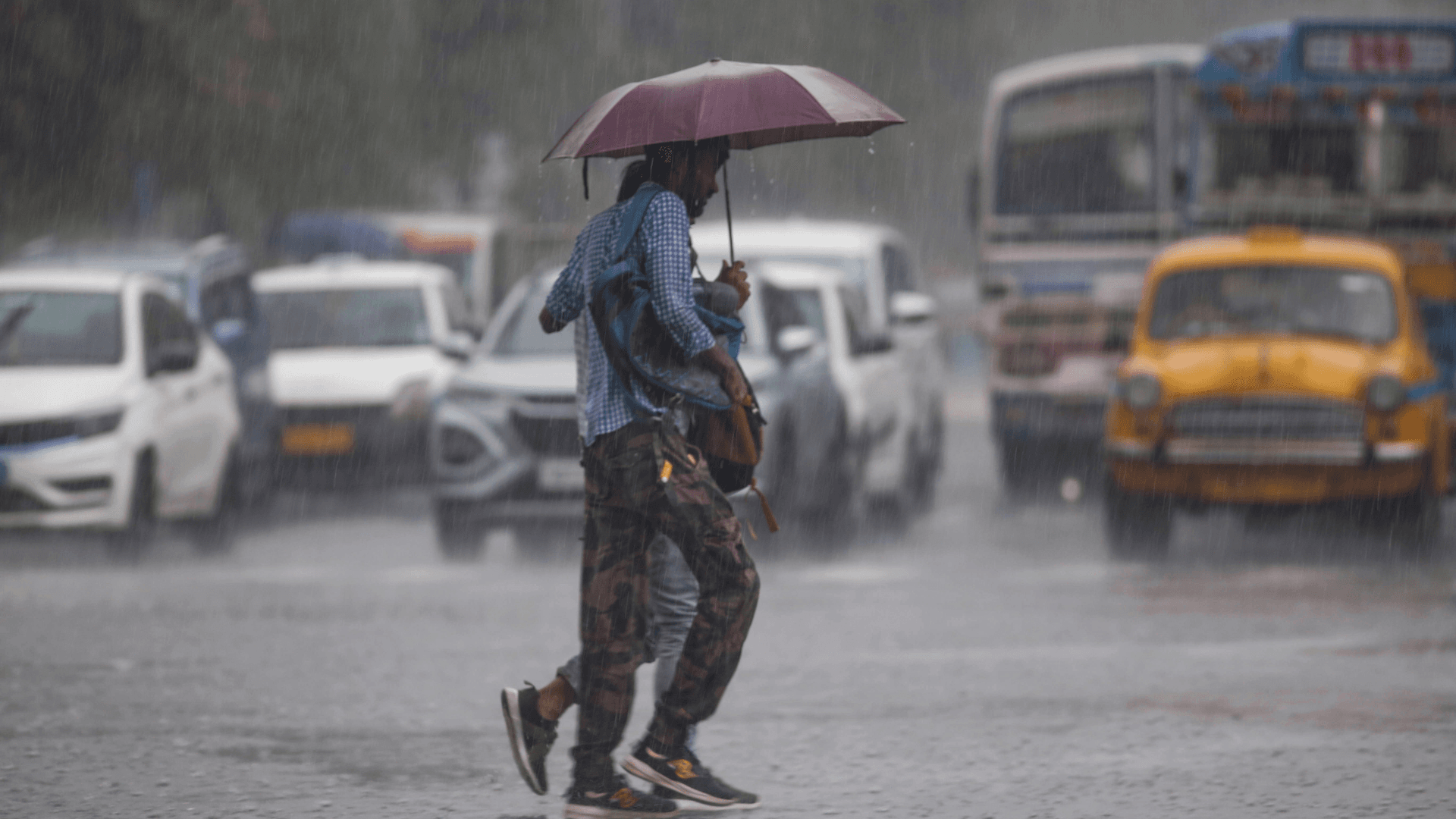 People cross a rain-soaked Kolkata road under an umbrella during heavy rainfall.